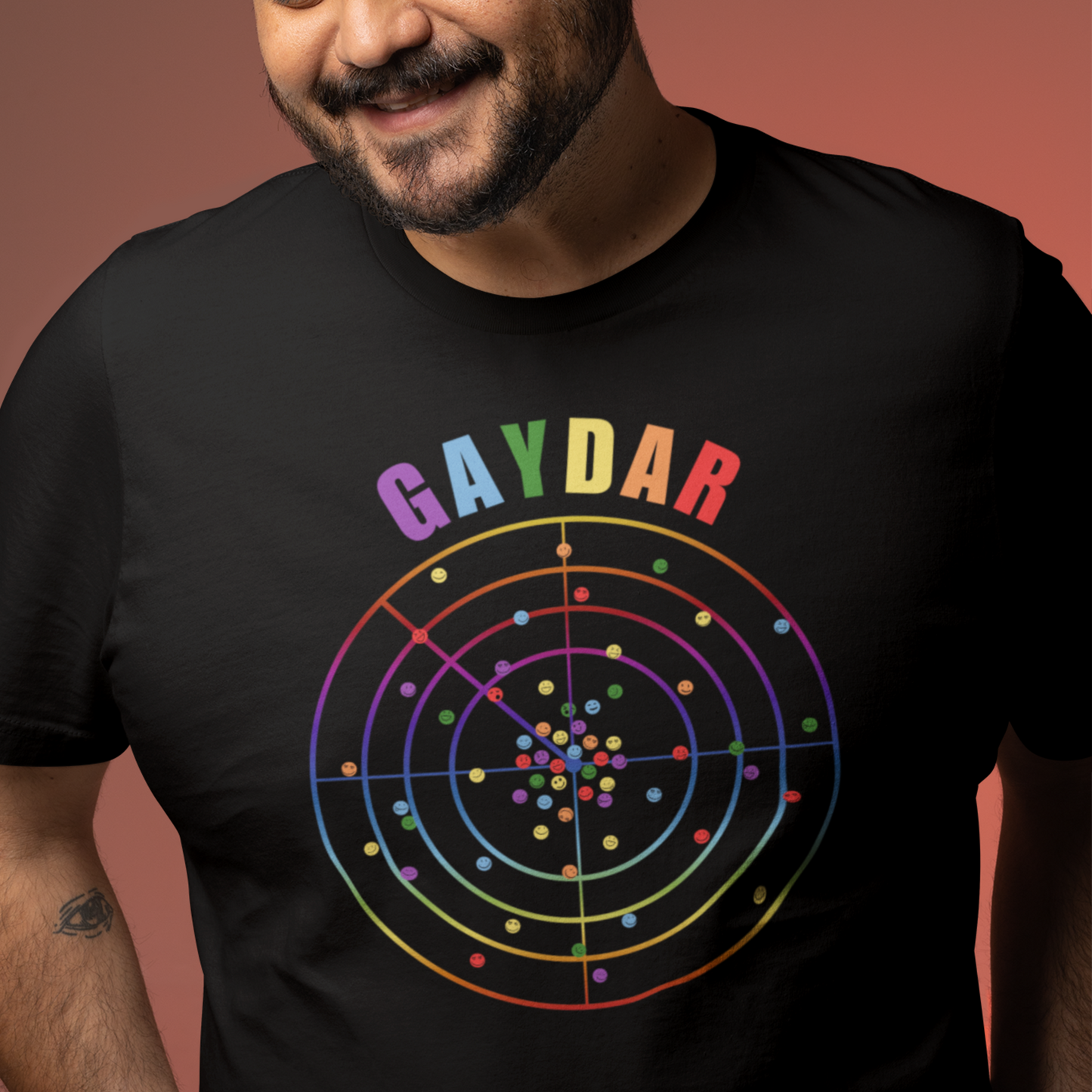 Happy man wearing a Black LGBTQ T-shirt with GAYDAR in pride colours and a graphic of a radar with lots of colourful dots on it with happy faces.