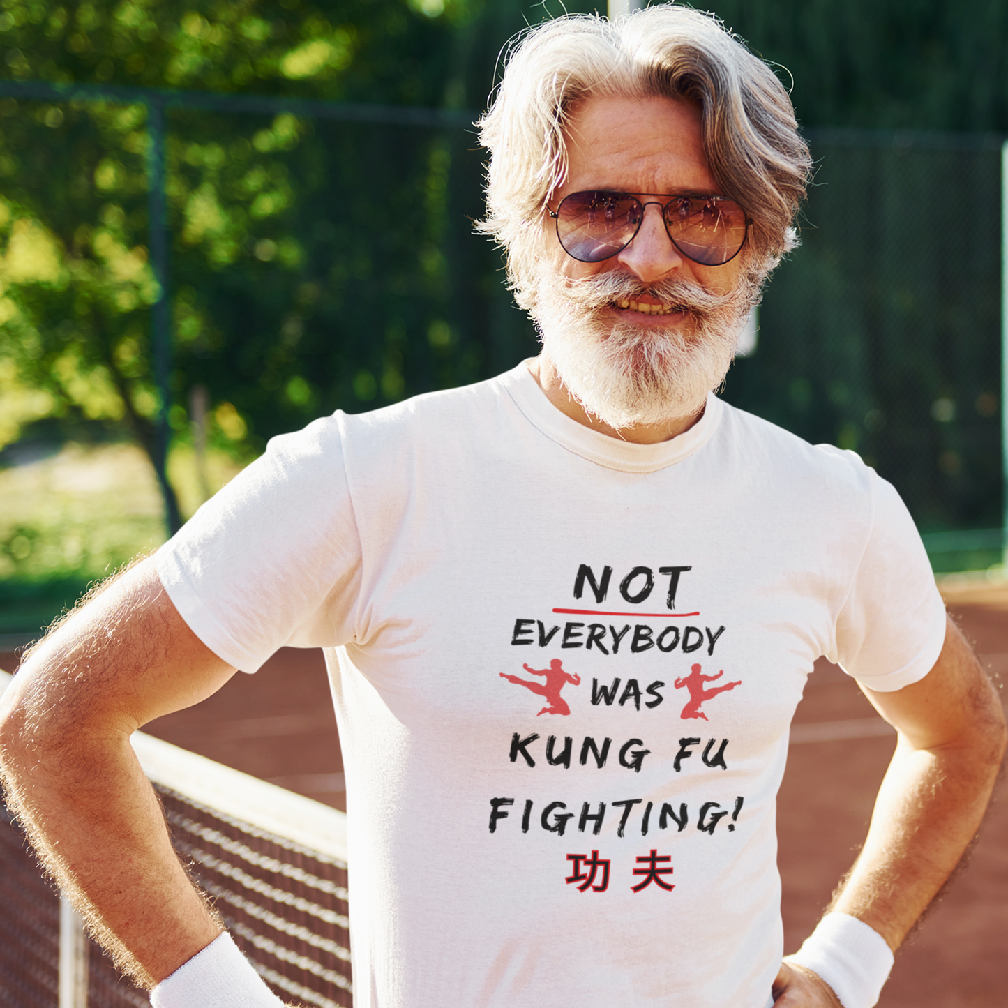 Older man on a tennis court wearing a white T-shirt with the text 'Not everybody was kung fu fighting' on the front