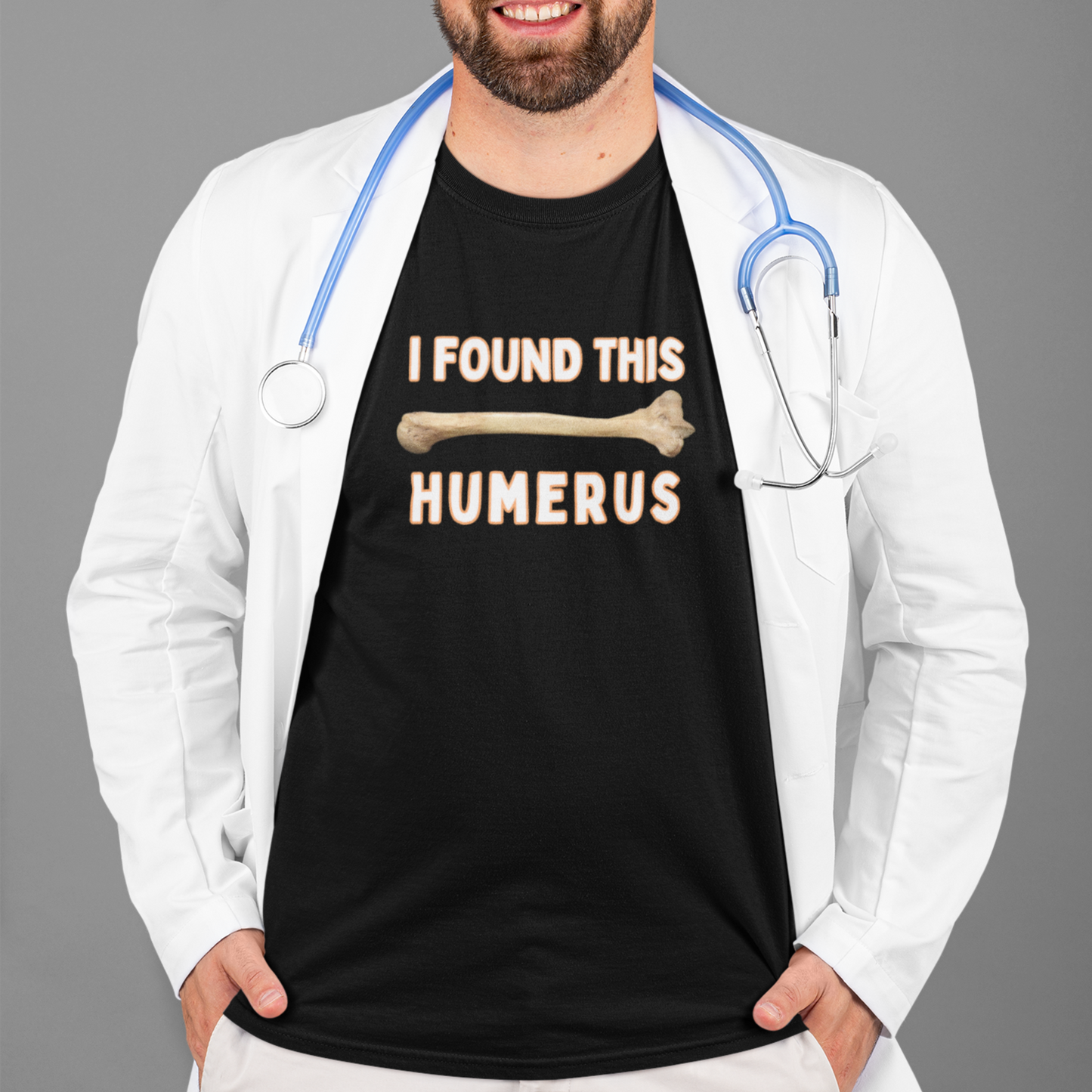 Funny T-shirt that has a arm bone on it and reads 'I found this humerus', modelled by a Doctor, T-shirt is black with white letters