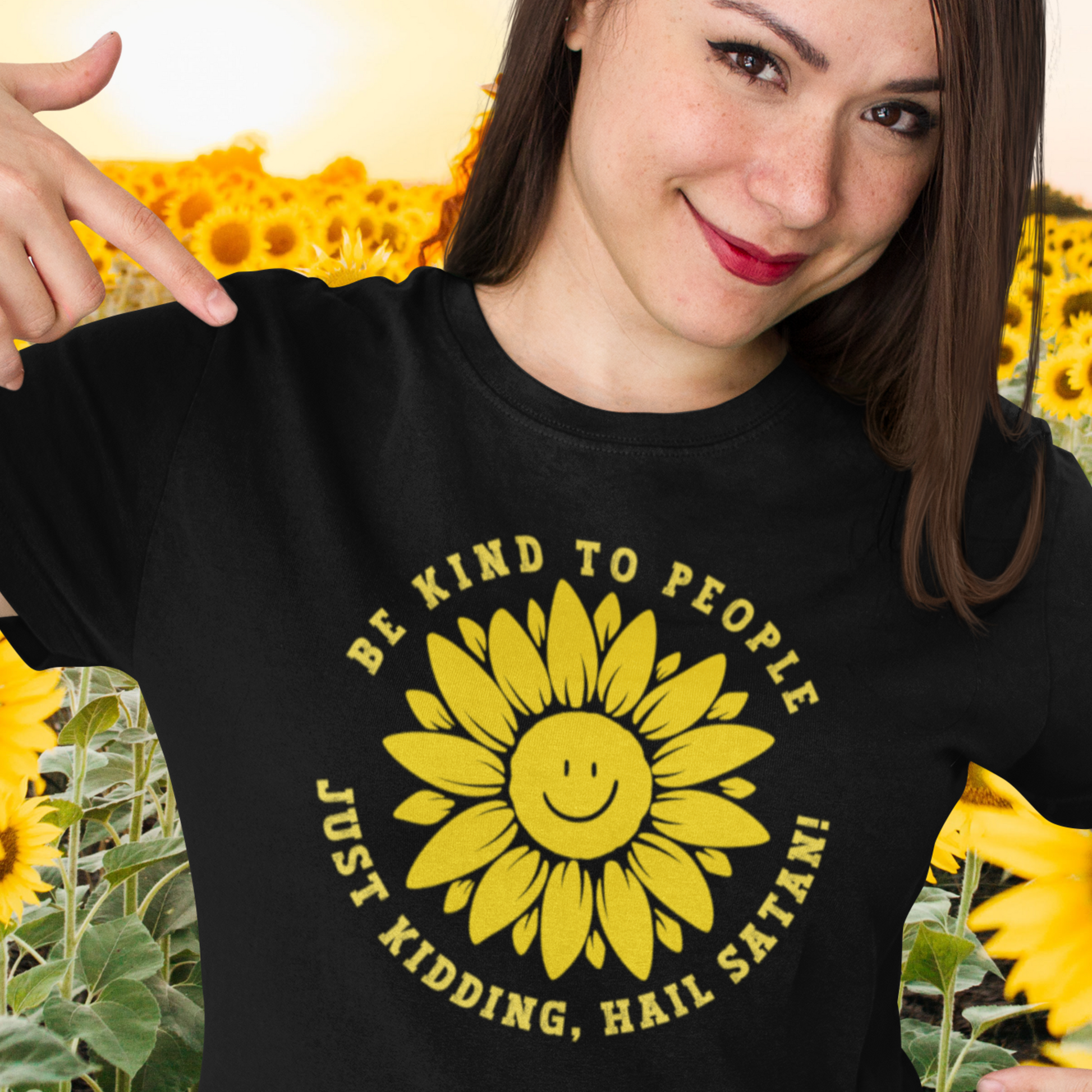 happy female in a sunflower field wearing a black Funny T-shirt with a smiling sunflower design and yellow text that reads, Be Kind To people, Just Kidding, Hail Satan!