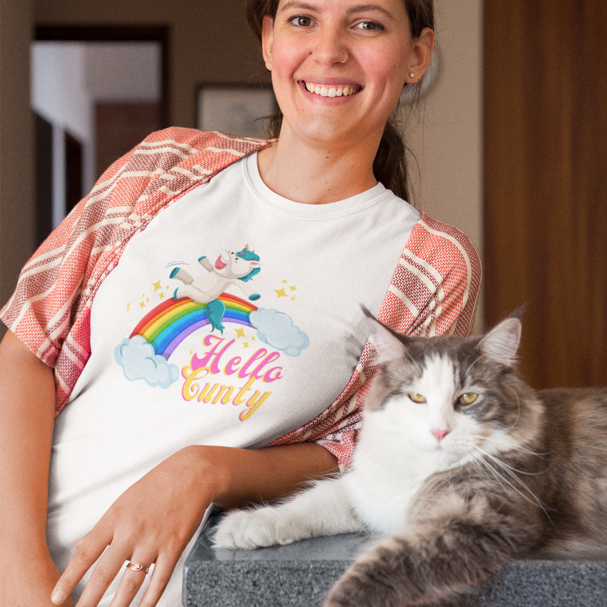 Amused young woman wearing a Possibly offensive T-shirt that has a unicorn sliding down a rainbow on it with text that reads Hello Cunty, in white.