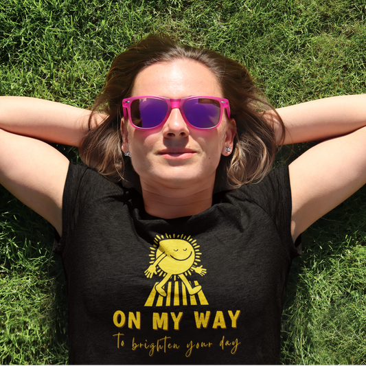 young woman sunbathing wearing a black T shirt with a walking sun that reads On My Way To Brighten Your Day