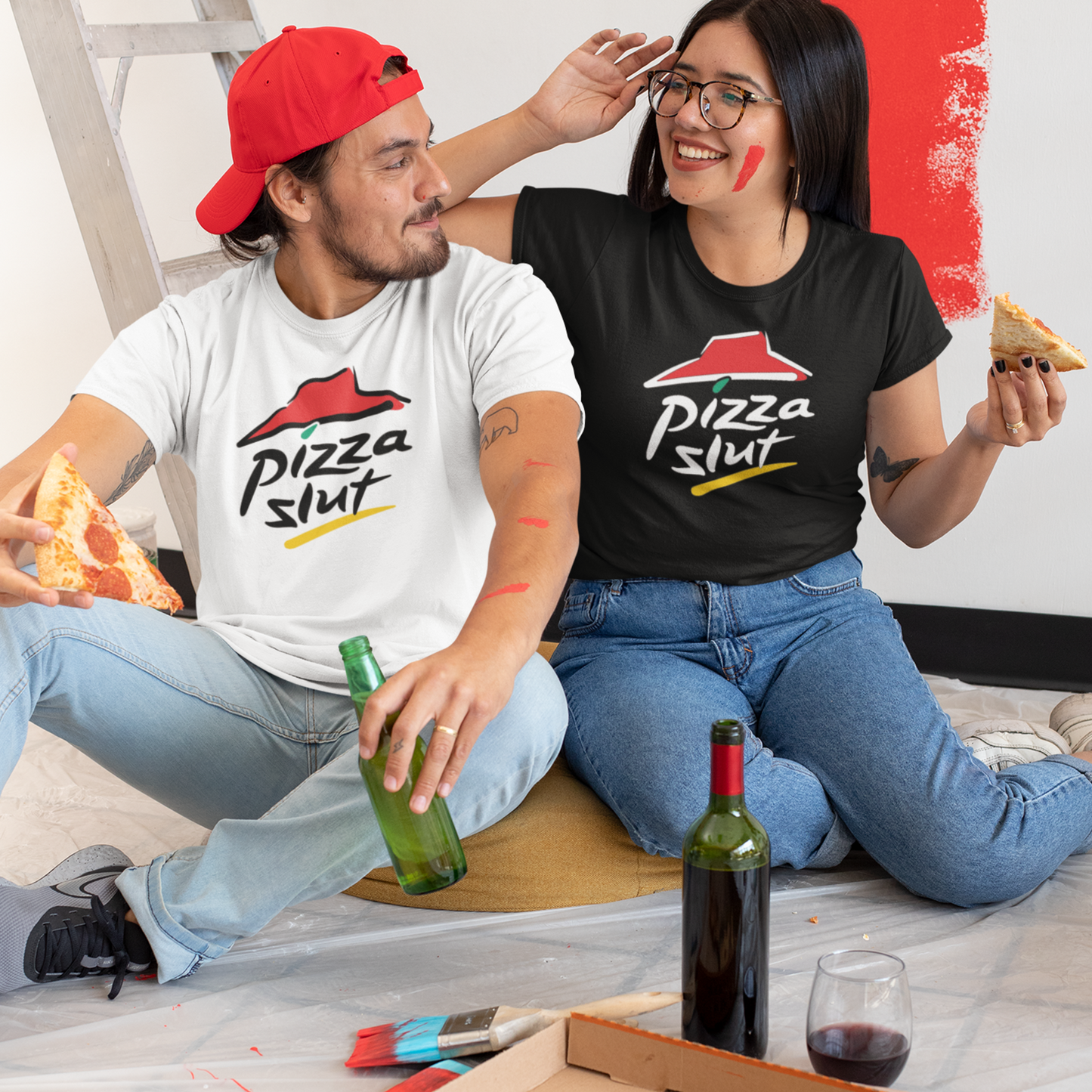 Couple sitting on the floor eating pizza wearing Pizza Slut T-shirts