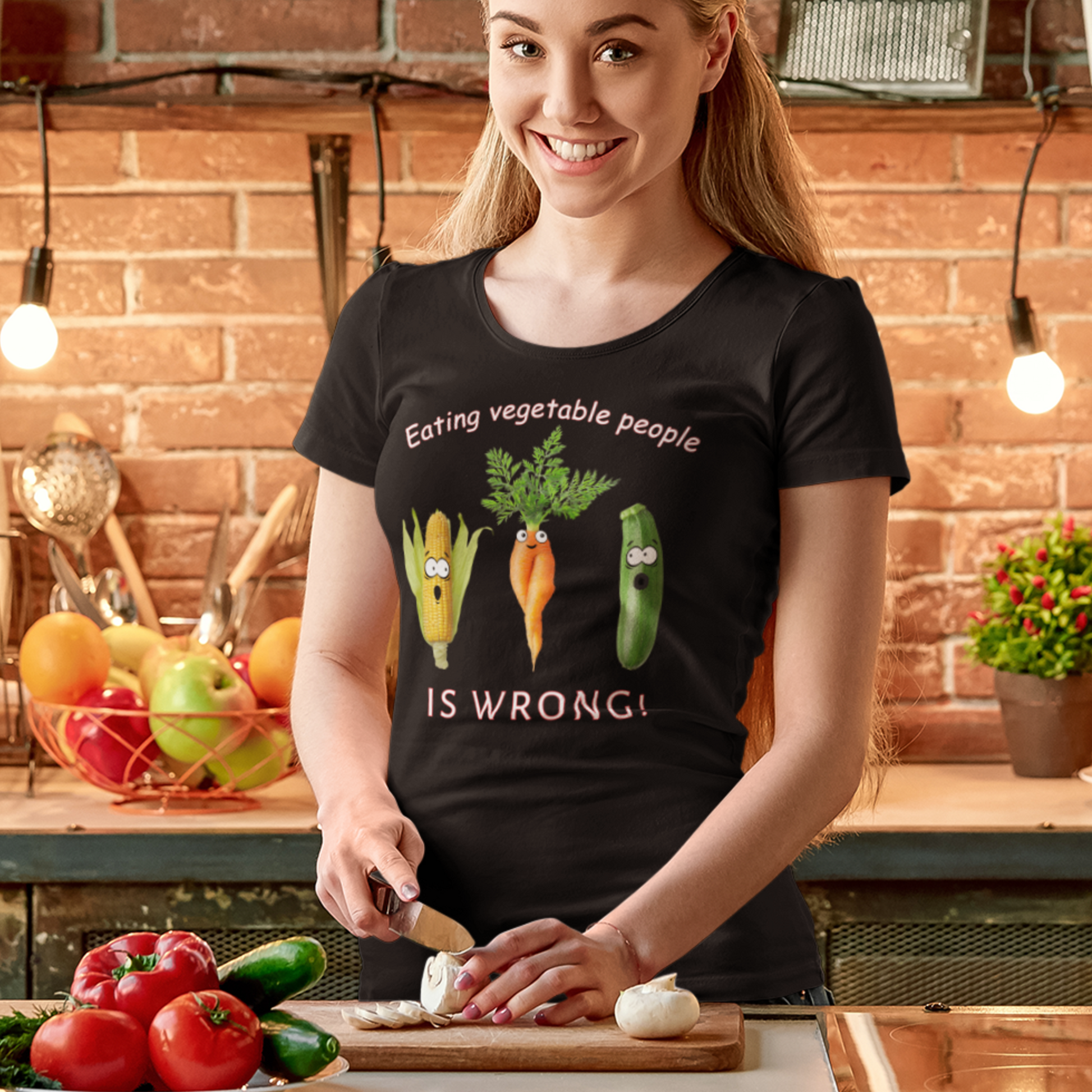 young woman laughing and cutting vegetables wearing a bleck Eating Vegetable People is Wrong! T-shirt with humanised vegetables.