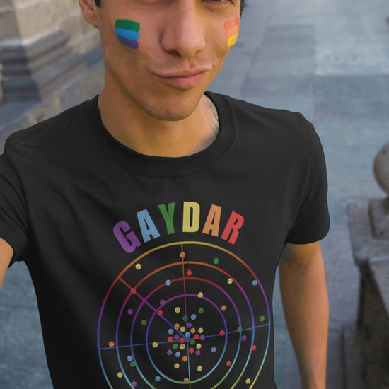 Video of young man at a pride rally wearing a Black LGBTQ T-shirt with GAYDAR in pride colours and a graphic of a radar with lots of colourful dots on it with happy faces.