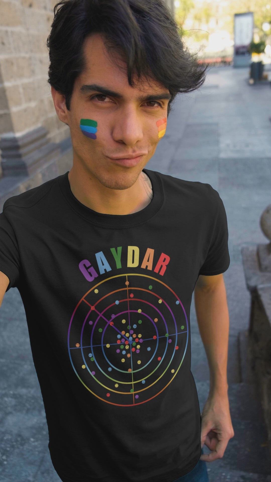 Video of young man at a pride rally wearing a Black LGBTQ T-shirt with GAYDAR in pride colours and a graphic of a radar with lots of colourful dots on it with happy faces.