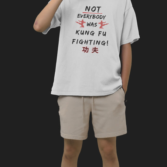 Young Asian man standing whilst drinking and eating wearing a white T-shirt that reads Not Everybody Was Kung Fu Fighting