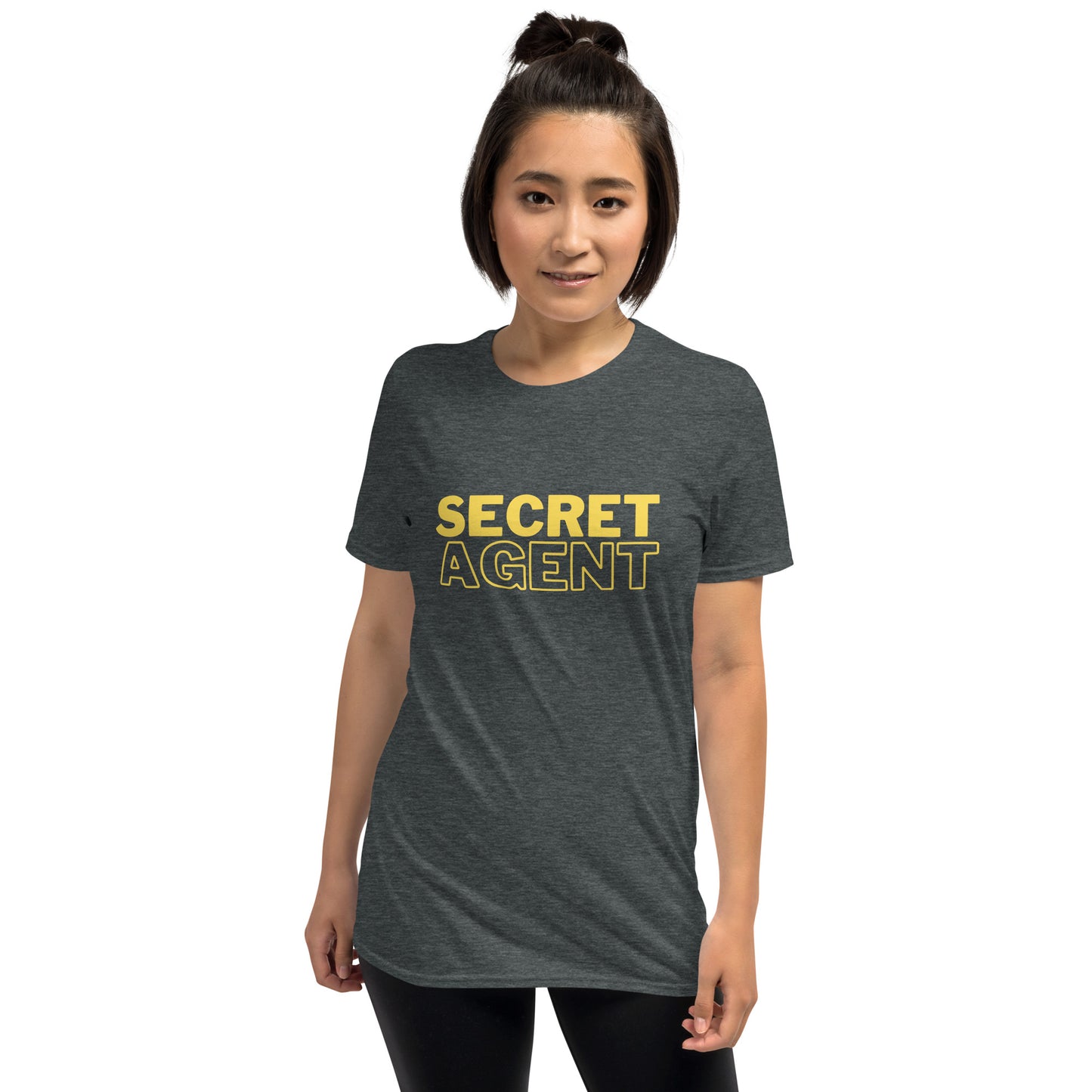 Amused female model wearing a Dark Heather Grey unisex T-shirt that reads SECRET AGENT in yellow text