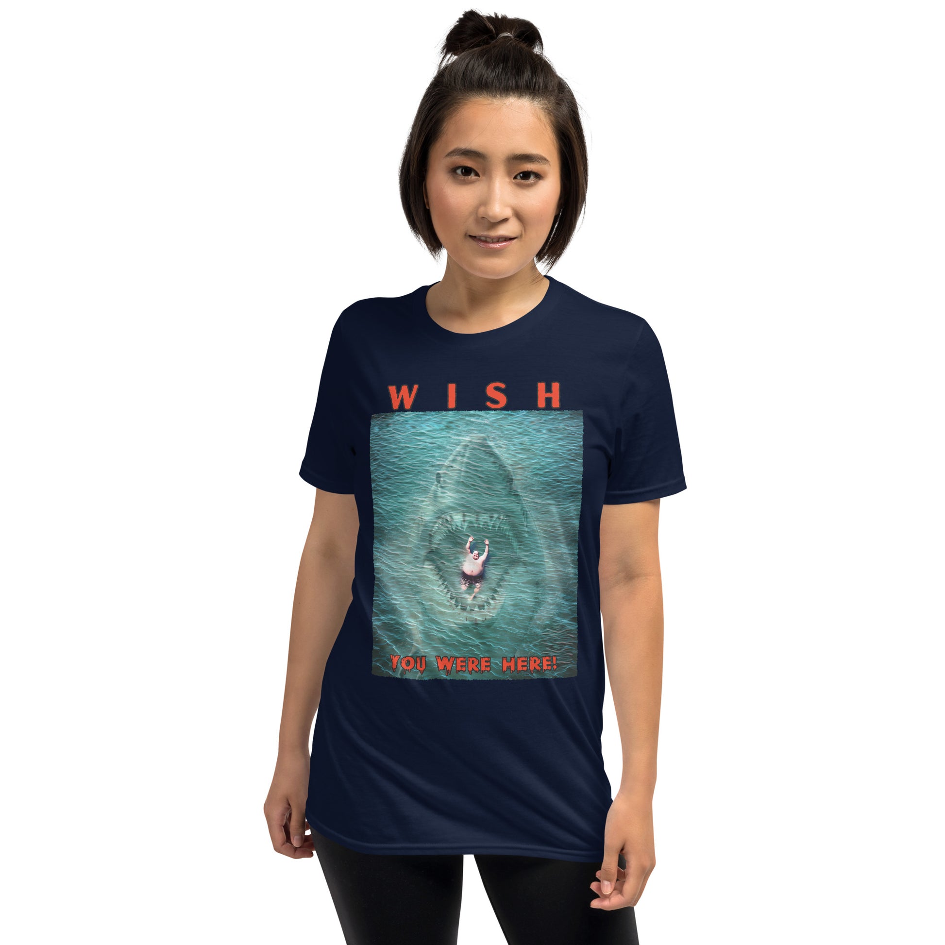 young woman wearing a navy funny T-shirt with an image of a fat guy floating in the sea, with a large shark with its jaws open coming up underneath him, text reads, Wish you were here