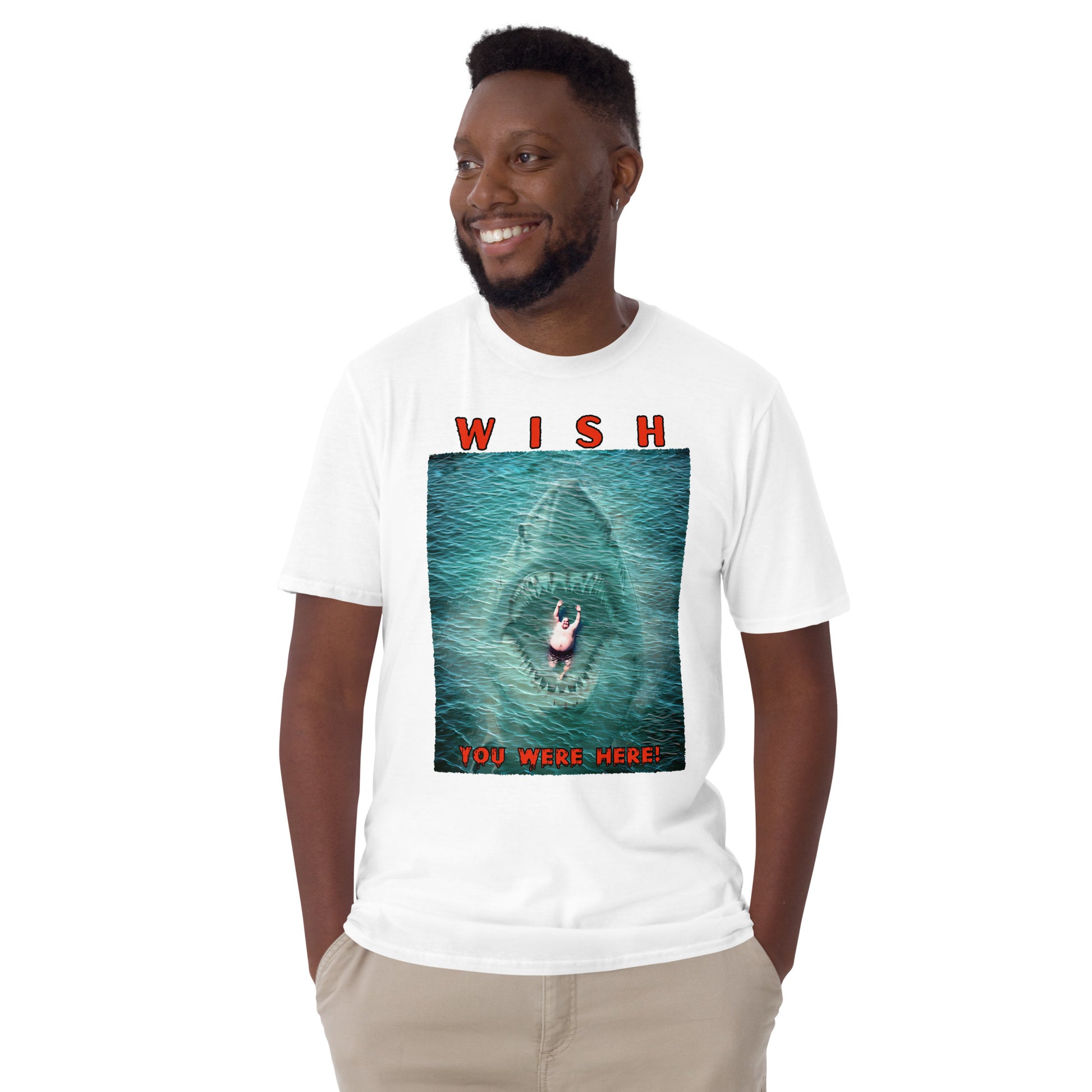 happy man wearing a white funny T-shirt with an image of a fat guy floating in the sea, with a large shark with its jaws open coming up underneath him, text reads, Wish you were here