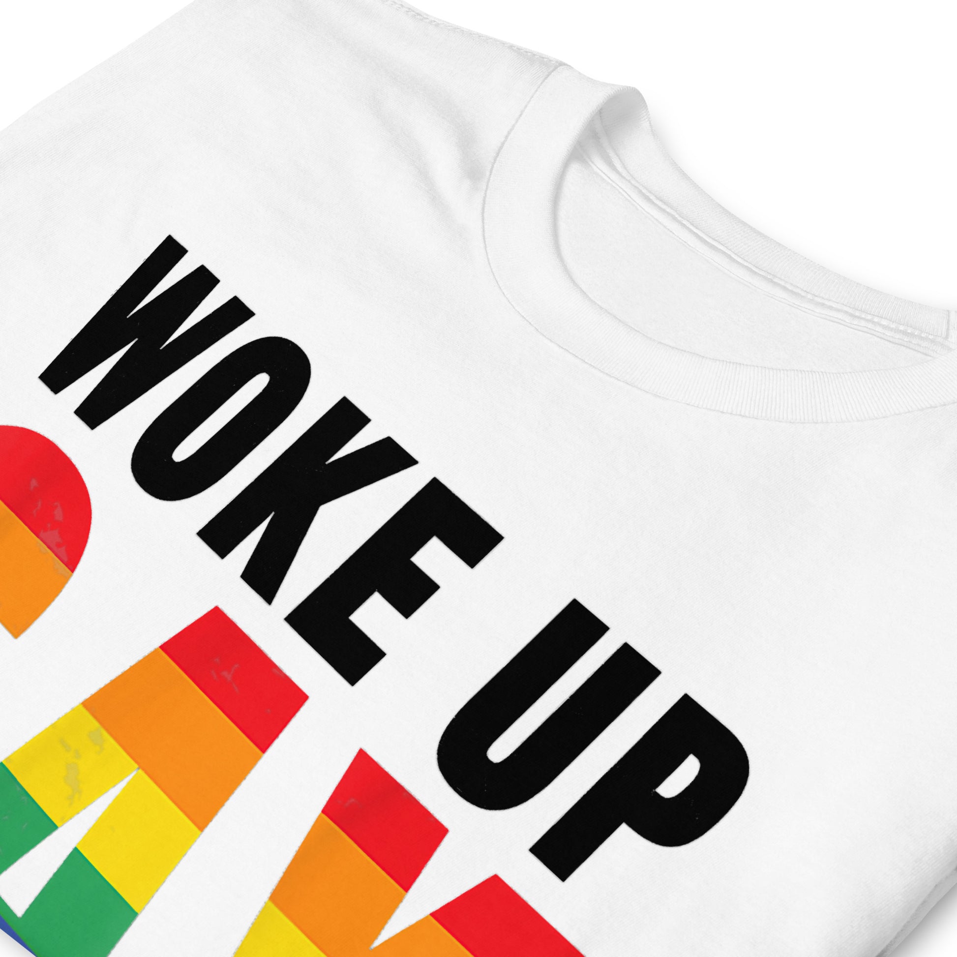 Folded white t-shirt that reads Woke Up Gay Again in pride colours